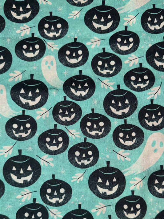 A close-up of a Halloween-themed fabric pattern featuring black jack-o'-lanterns, white ghosts, and small bats on a light aqua background.
