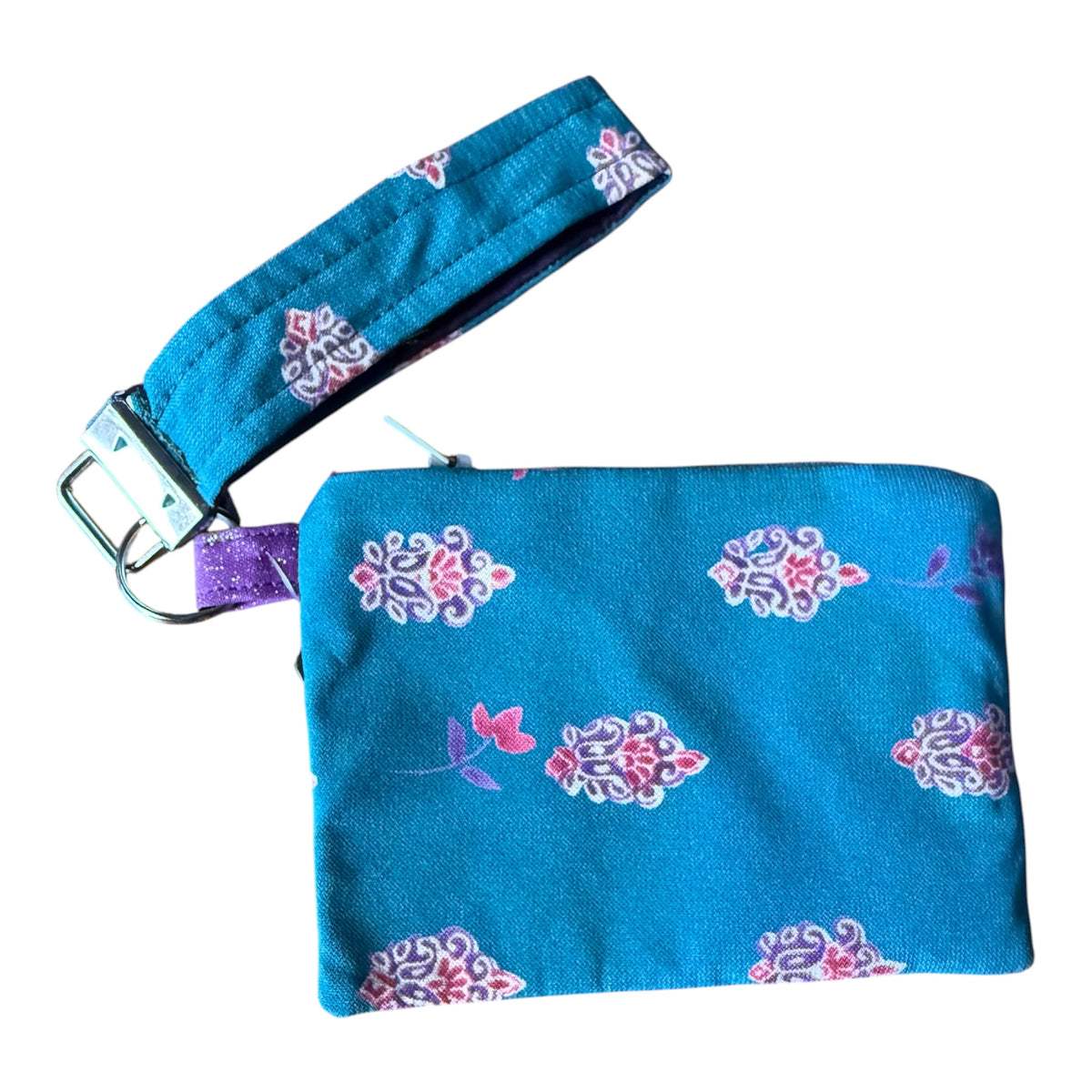 A teal blue fabric wristlet pouch with a matching wrist strap, decorated with pink and purple floral patterns, shown on a plain white background.